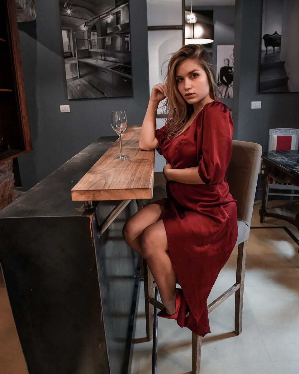 Woman in a burgundy velvet dress with puffed sleeves at a bar counter