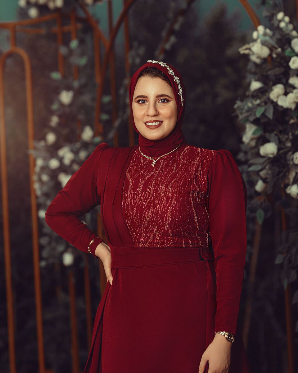 Smiling woman in a long-sleeve burgundy lace gown with floral decor