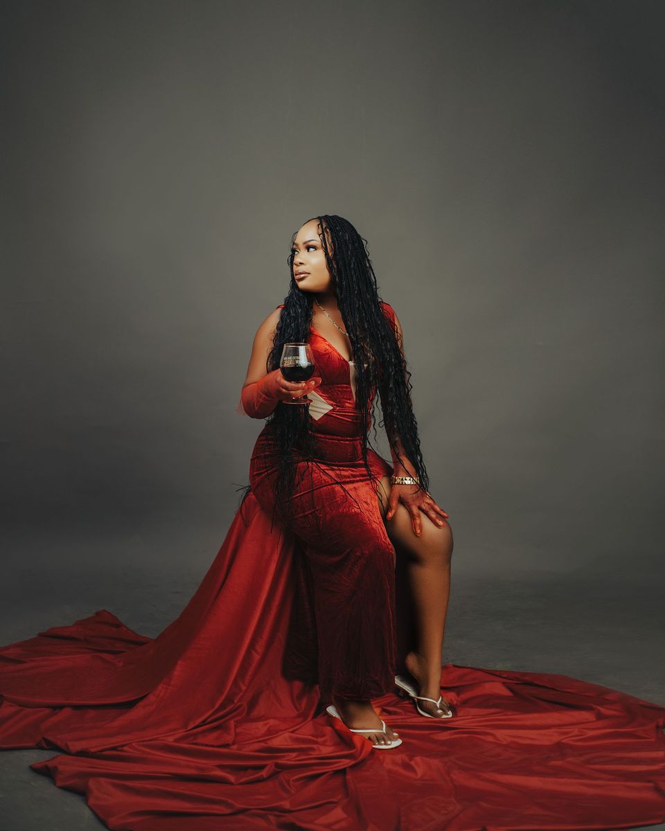 Woman in a strapless red-burgundy gown with a long train holding a wine glass