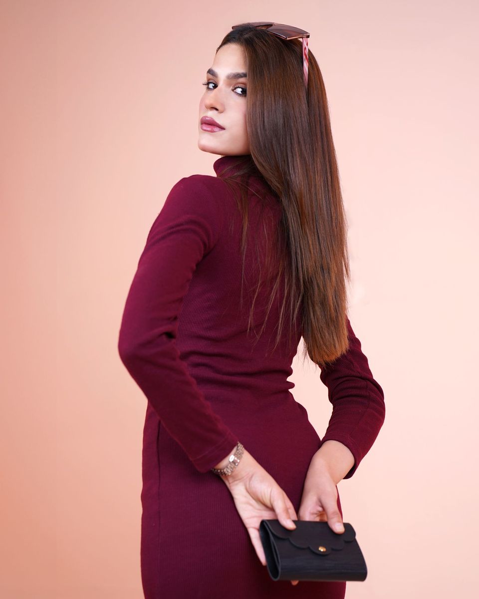 Woman in a burgundy mock-neck long-sleeve dress holding a small wallet