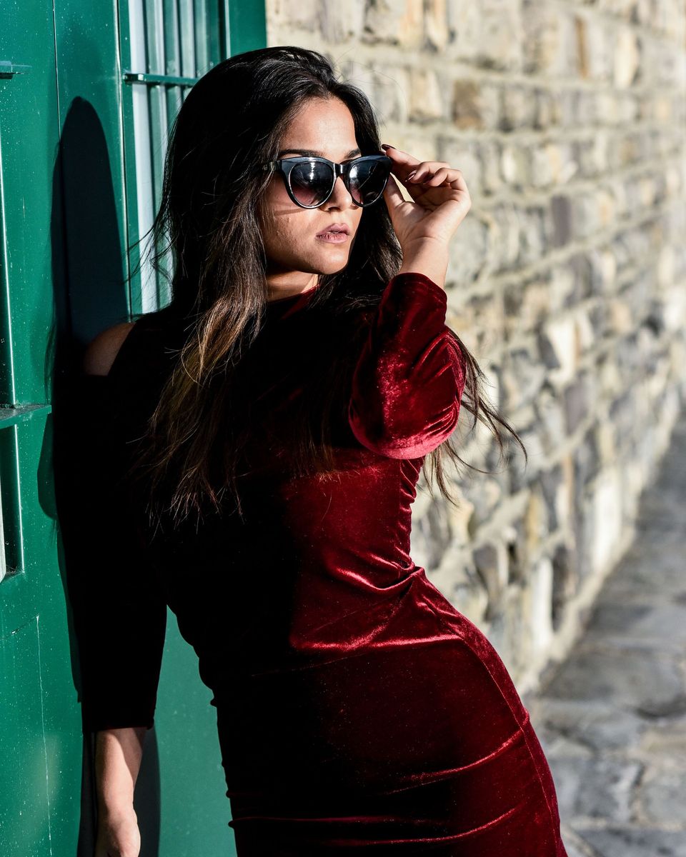 Woman in a burgundy velvet wrap mini dress posing by a stone wall