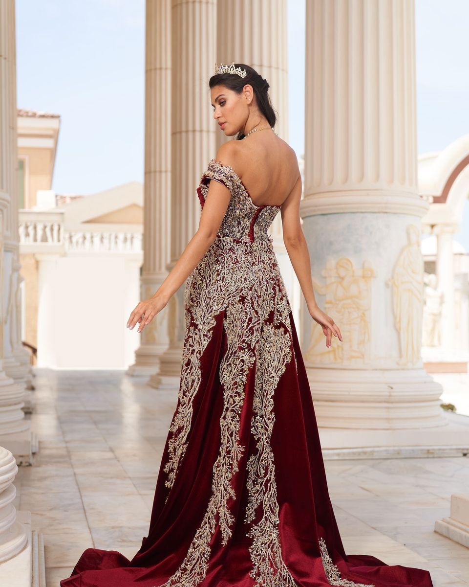 Woman in an embellished burgundy mermaid gown among classical columns