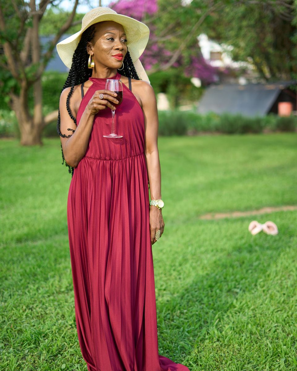 Woman in a flowing burgundy halter maxi dress and sun hat in a park